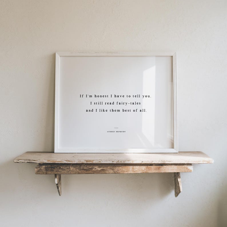 May include: A framed print with a white border displays a quote in black text: "If I'm honest I have to tell you. I still read fairy-tales and I like them best of all." The print rests on a rustic wooden shelf.
