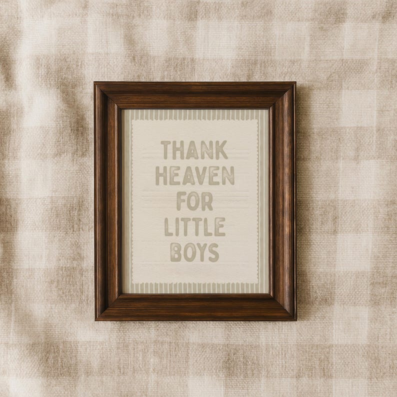 Puede incluir: Un marco de madera marr&oacute;n oscuro que contiene una impresi&oacute;n con el texto "THANK HEAVEN FOR LITTLE BOYS" en gris. El fondo es beige claro con un patr&oacute;n sutil. Es un objeto decorativo.