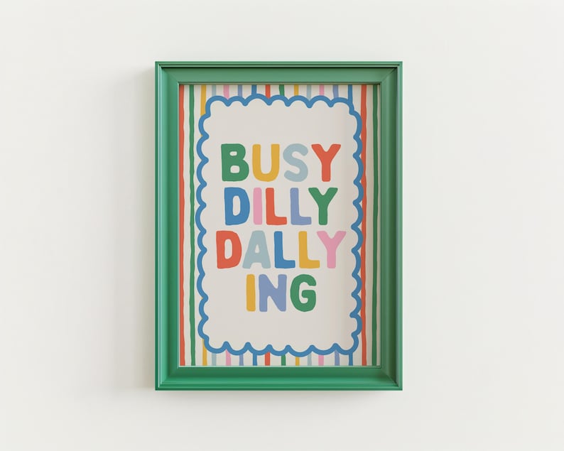 May include: A framed art print with the words "BUSY DILLY DALLYING" in colorful block letters. The print has a white background with a scalloped border and is framed in a green frame. The background has vertical stripes.