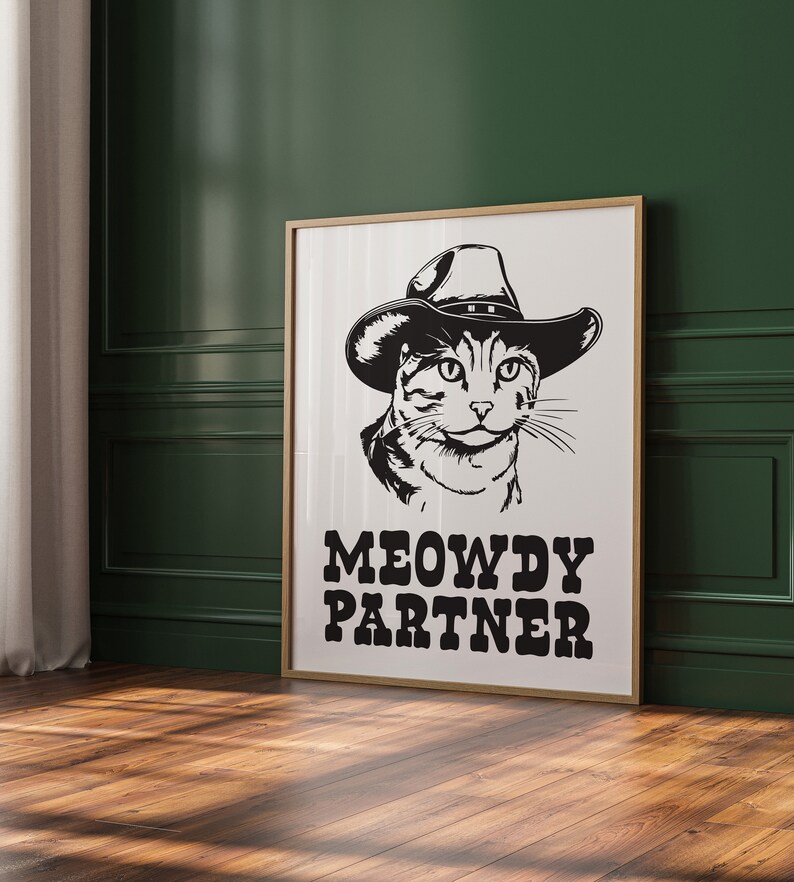 Pu&ograve; includere: Illustrazione in bianco e nero di un gatto con un cappello da cowboy. Il testo "MEOWDY PARTNER" &egrave; sotto il gatto.