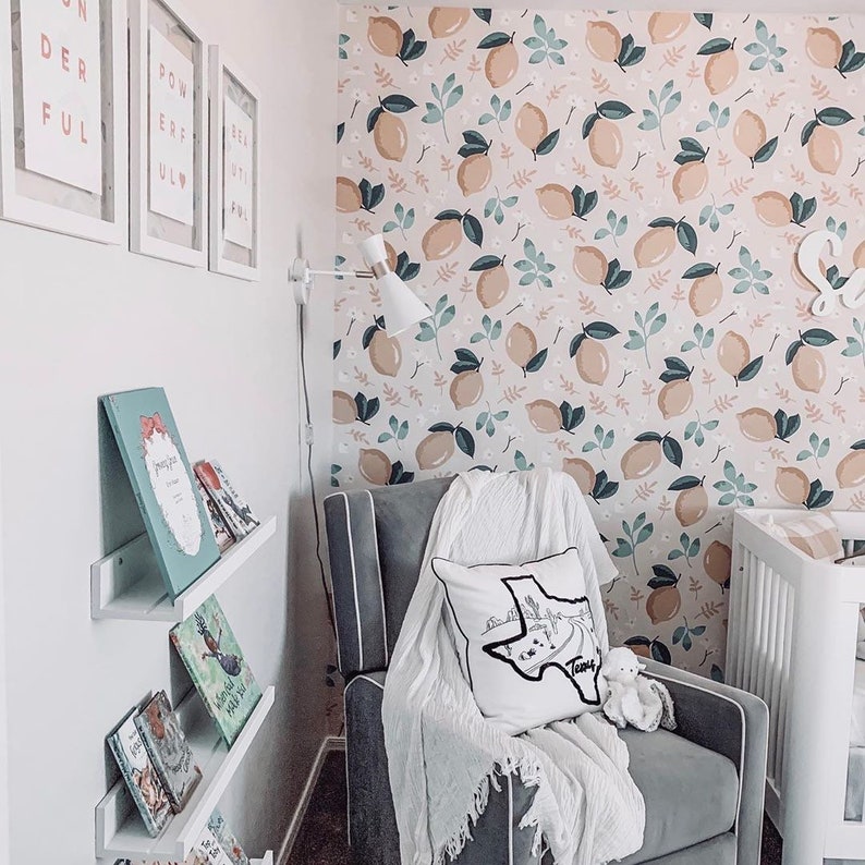 May include: A gray armchair with a white throw blanket and a white pillow with a black outline of the state of Texas and the word "Texas" on it. The armchair is in front of a wall with a lemon-themed wallpaper. There are books on a shelf to the left of the armchair.