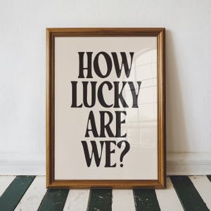 May include: A framed print with the text "How lucky are we?" in black bold letters on a cream background.