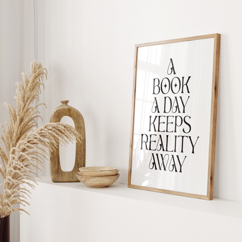 May include: A framed print with the text "A book a day keeps reality away" in black lettering on a white background. The frame is made of wood and has a natural finish.