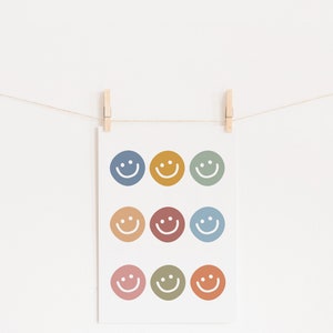May include: A white card with nine colorful smiley faces printed on it. The card is hanging on a string with wooden clothespins.