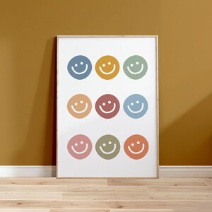 May include: A framed print with nine colorful smiley faces arranged in a grid pattern. The background is white and the frame is light wood.