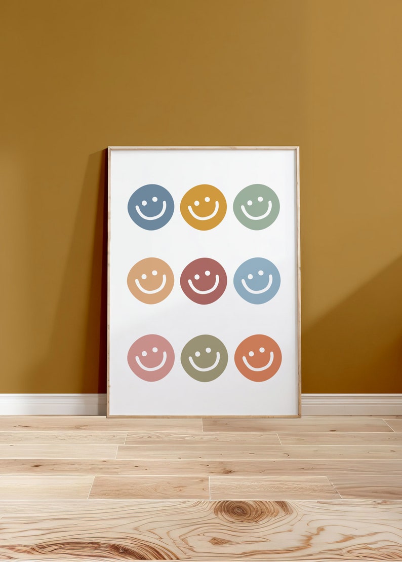 May include: A framed print with nine colorful smiley faces arranged in a grid pattern. The background is white and the frame is light wood.