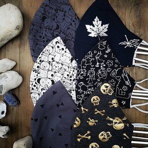 May include: Six different fabric face masks with various patterns. The masks are made of a soft, breathable fabric and feature a variety of designs, including animals, skulls, and geometric shapes. The masks are all in shades of gray and black.