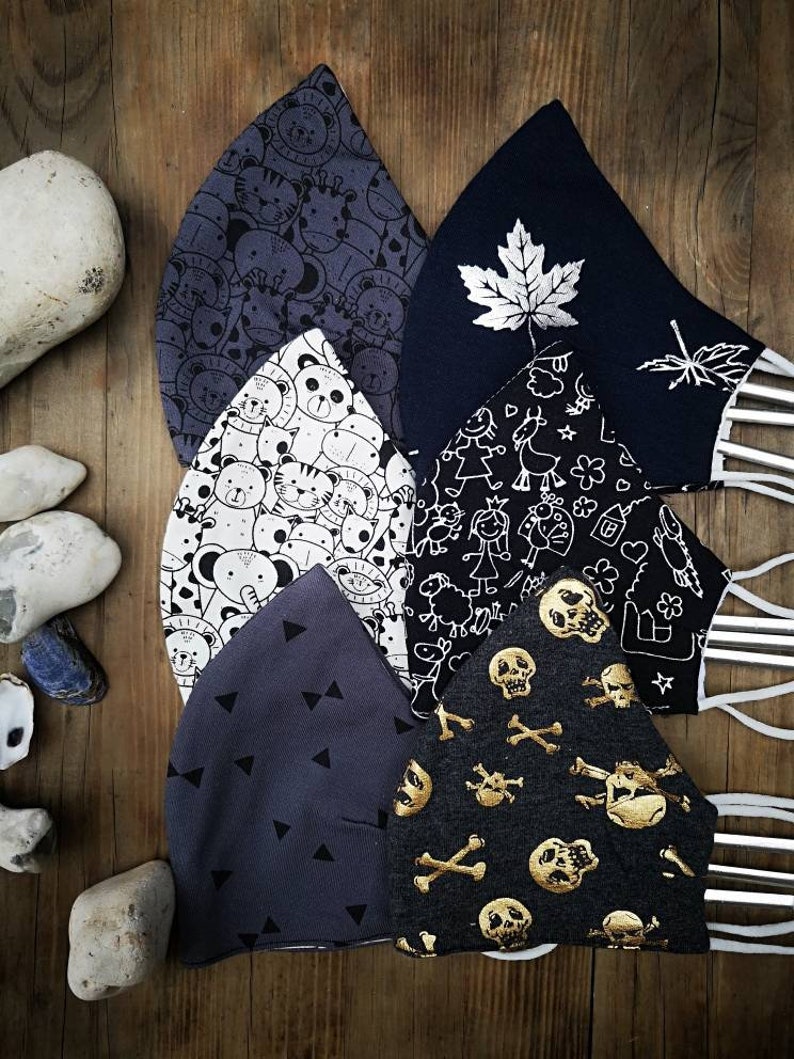 May include: Six different fabric face masks with various patterns. The masks are made of a soft, breathable fabric and feature a variety of designs, including animals, skulls, and geometric shapes. The masks are all in shades of gray and black.