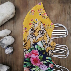 May include: Three reusable face masks with different patterns. The top mask is yellow with a floral print, the middle mask is yellow with a meerkat print, and the bottom mask is dark blue with a floral print.