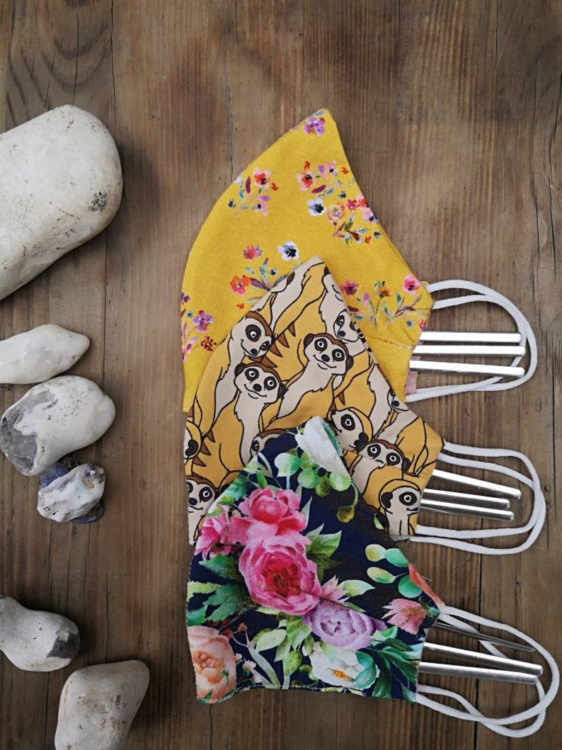 May include: Three reusable face masks with different patterns. The top mask is yellow with a floral print, the middle mask is yellow with a meerkat print, and the bottom mask is dark blue with a floral print.