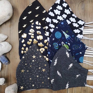 May include: Six different fabric face masks with various patterns. The masks are black, gray, and blue with gold and white accents. The patterns include lightning bolts, stars, clouds, planets, and rockets.