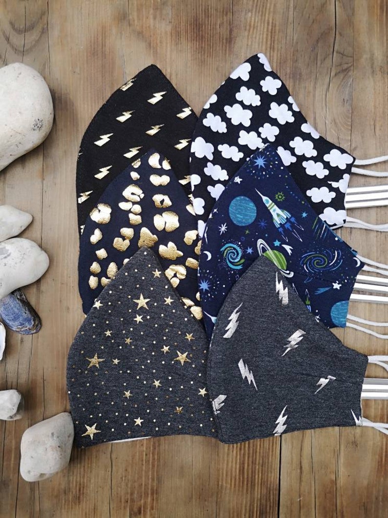 May include: Six different fabric face masks with various patterns. The masks are black, gray, and blue with gold and white accents. The patterns include lightning bolts, stars, clouds, planets, and rockets.