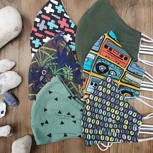 May include: Six different fabric face masks with various patterns. The masks are green, black, white, blue, yellow, and orange. The patterns include geometric shapes, cassette tapes, and coffee beans.