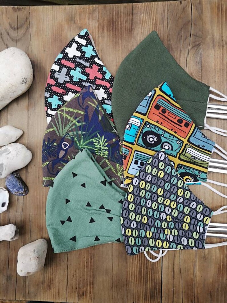 May include: Six different fabric face masks with various patterns. The masks are green, black, white, blue, yellow, and orange. The patterns include geometric shapes, cassette tapes, and coffee beans.