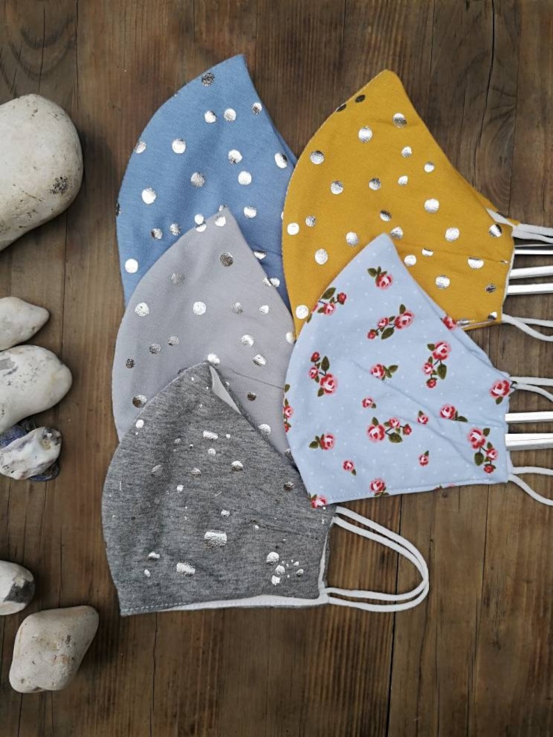 May include: Five fabric face masks with different patterns. The masks are all light blue, gray, or yellow with silver polka dots or a floral pattern. The masks are all made of a soft, breathable fabric.