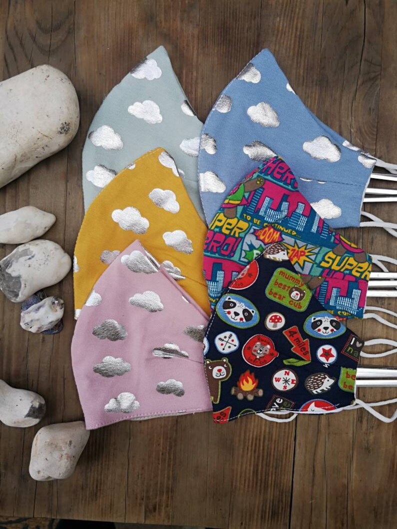 May include: Five fabric face masks with different patterns. The masks are all made of a soft, cotton fabric and have adjustable ear loops. The patterns include clouds with silver accents, a cityscape with the text "To Be Continued..." and "Super Pro!" and a camping theme with a variety of colorful patches.