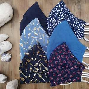 May include: Six different fabric face masks with various patterns. The masks are blue, black, and red with white, gold, and silver accents. The patterns include arrows, leaves, and floral designs.