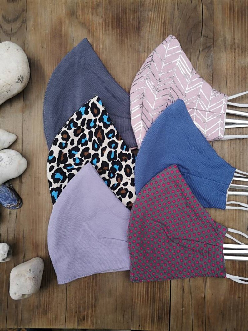 May include: Six different fabric face masks. The masks are all made of cotton and have different patterns. The patterns include a gray solid, a pink chevron, a blue solid, a brown and blue leopard print, a purple solid, and a gray with pink polka dots.