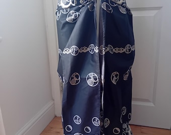May include: A black wrap skirt featuring a repeating white pattern of circular spiral motifs and horizontal geometric bands. The garment is tied at the waist with a fabric knot, creating a draped silhouette that falls to the lower legs.