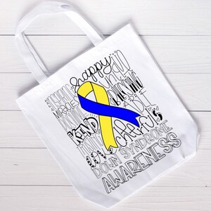 May include: White tote bag with a yellow and blue ribbon and the words "Happy, Unique, Blessings, Kind, Strong, Love, Cherish, Down Syndrome, Awareness" printed in black.
