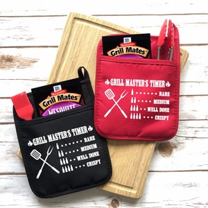 May include: Two black and red oven mitts with pockets. The mitts have a white design that says "Grill Master's Timer" with a graphic of crossed grilling tools and a list of doneness levels for meat. The pockets contain packets of grill seasoning and grilling tools.