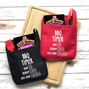 May include: Two black and red oven mitts with pockets. The mitts have the text "BBQ TIMER" and a graphic of beer mugs with the words "RARE", "MEDIUM", and "WELL DONE" printed below.