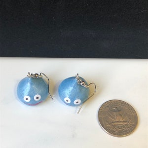 May include: A pair of blue slime earrings with white eyes and a red mouth. The earrings are about the size of a US quarter.