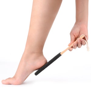 May include: A person using a wooden foot scrubber with a black abrasive surface to exfoliate their heel.