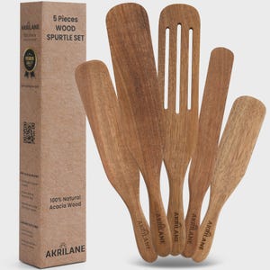 May include: A set of five wooden spatulas and a slotted spatula made of acacia wood. The spatulas are various shapes and sizes, with the brand name "AKRILANE" printed on the handles. The set comes in a cardboard box that reads "5 Pieces Wood Spurtle Set."