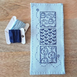 Könnte beinhalten: Ein blaues und weißes Kreuzstichmuster mit vier verschiedenen Designs. Die Designs beinhalten Koffer, Flugzeuge, Blumen und ein geometrisches Muster. Der Kreuzstich ist auf einem hellblauen Stoff.