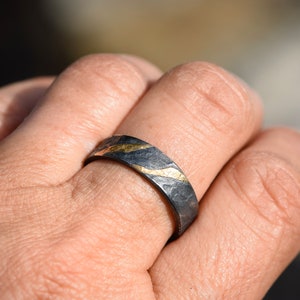 May include: A black and gold ring with a textured finish. The ring has a thin band with a wavy gold design.