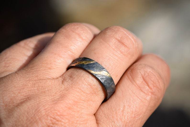 May include: A black and gold ring with a textured finish. The ring has a thin band with a wavy gold design.