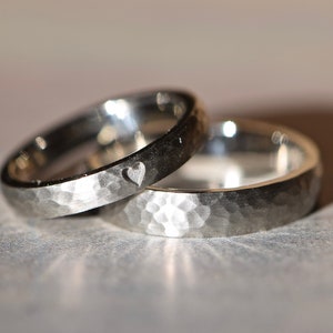 May include: Two silver wedding bands with a hammered finish. One band has a small heart engraved on the inside.