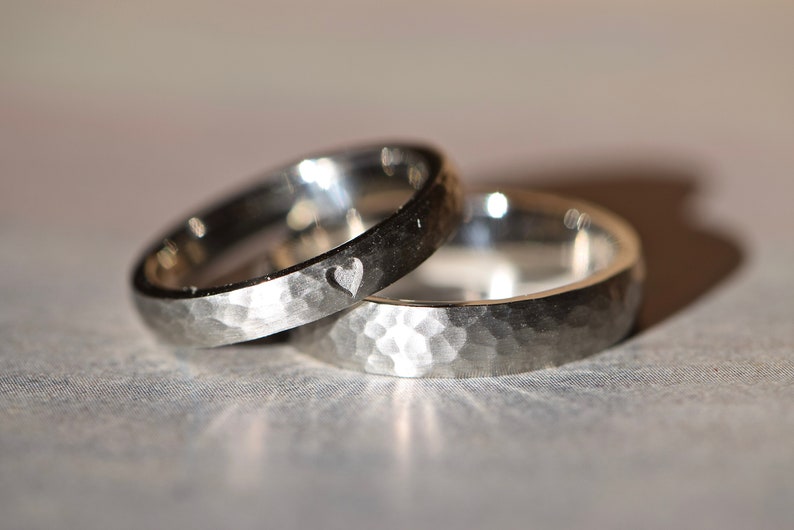 May include: Two silver wedding bands with a hammered finish. One band has a small heart engraved on the inside.