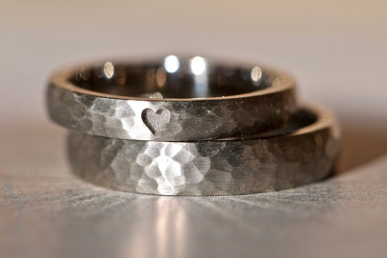 May include: Two silver hammered wedding bands with a heart cutout detail.