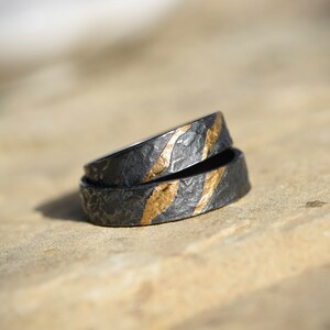 May include: Two black rings with gold accents. The rings are stacked on top of each other. The rings have a textured surface.