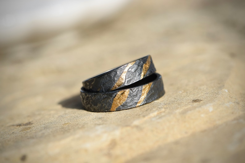 May include: Two black rings with gold accents. The rings are stacked on top of each other. The rings have a textured surface.