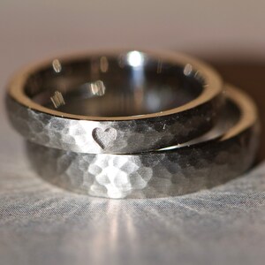 May include: Two silver wedding bands with a hammered finish. The top band has a small heart engraved on the inside.
