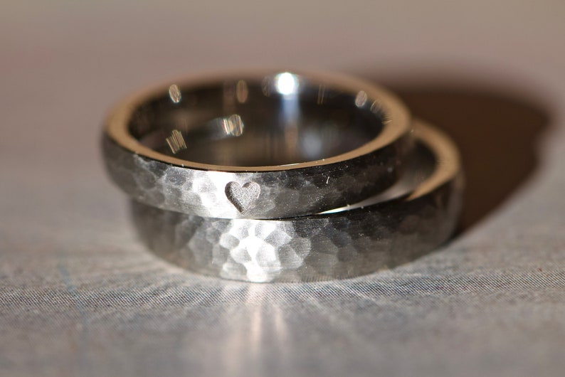 May include: Two silver wedding bands with a hammered finish. The top band has a small heart engraved on the inside.