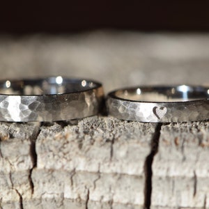 May include: Two silver wedding bands with a hammered texture. One band has a small heart cutout.