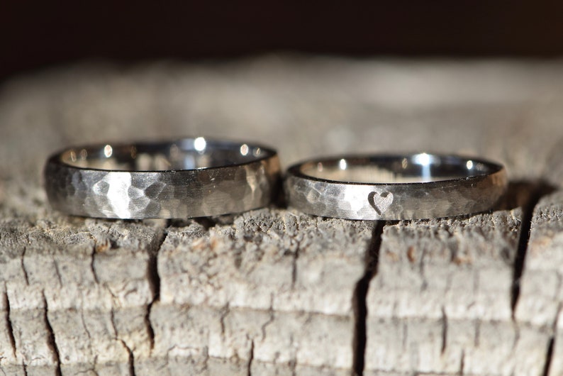 May include: Two silver wedding bands with a hammered texture. One band has a small heart cutout.