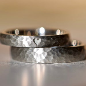 May include: Two silver wedding bands with a hammered finish. The top band has a small heart cutout.