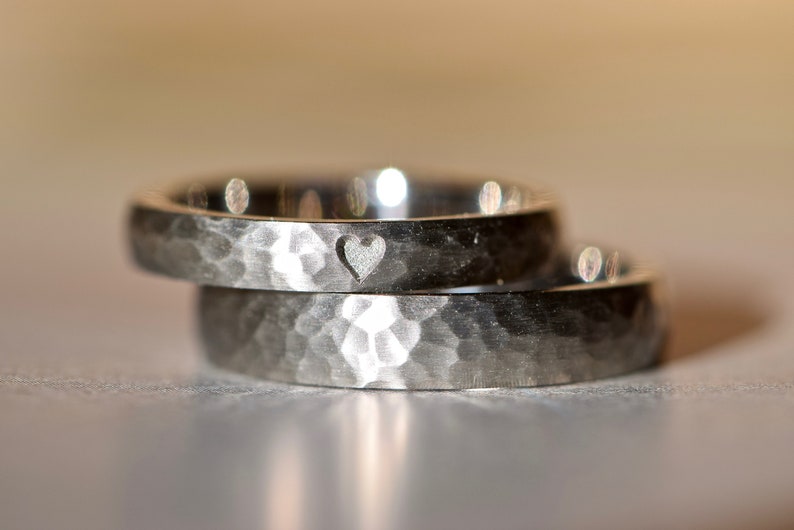May include: Two silver wedding bands with a hammered finish. The top band has a small heart cutout.