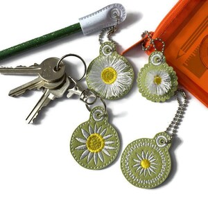 May include: Four green and white daisy keychains with silver chains. The keychains are attached to a set of keys and a pencil.
