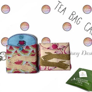 Könnte beinhalten: Zwei Teebeutel-Etuis, eines mit Wassermelonen-Print und das andere mit Flamingo-Print. Beide Etuis haben einen Knopfverschluss und eine Schlaufe für einen Schlüsselanhänger. Ein Teebeutel ist in der rechten unteren Ecke des Bildes zu sehen. Der Teebeutel ist grün und hat den Text "English Afternoon Tea" aufgedruckt.