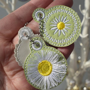 May include: Two green leather keyrings with white daisy embroidery. The keyrings are attached to a silver chain.