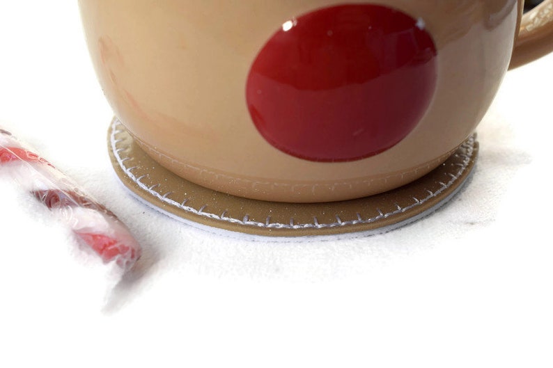 May include: A brown ceramic mug with a red circle design sits on a brown and white coaster. The mug has a handle and is partially visible.