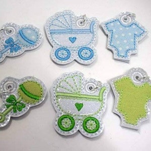 May include: Six embroidered iron-on patches for baby clothing. The patches feature a baby carriage, a rattle, and a onesie in blue and green.