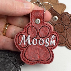 May include: Red leather paw print keyring with the name "Moosh" embroidered in white thread.