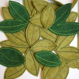 May include: A collection of felt leaves in shades of green and brown. The leaves are sewn together with a green thread, creating a decorative garland or embellishment.